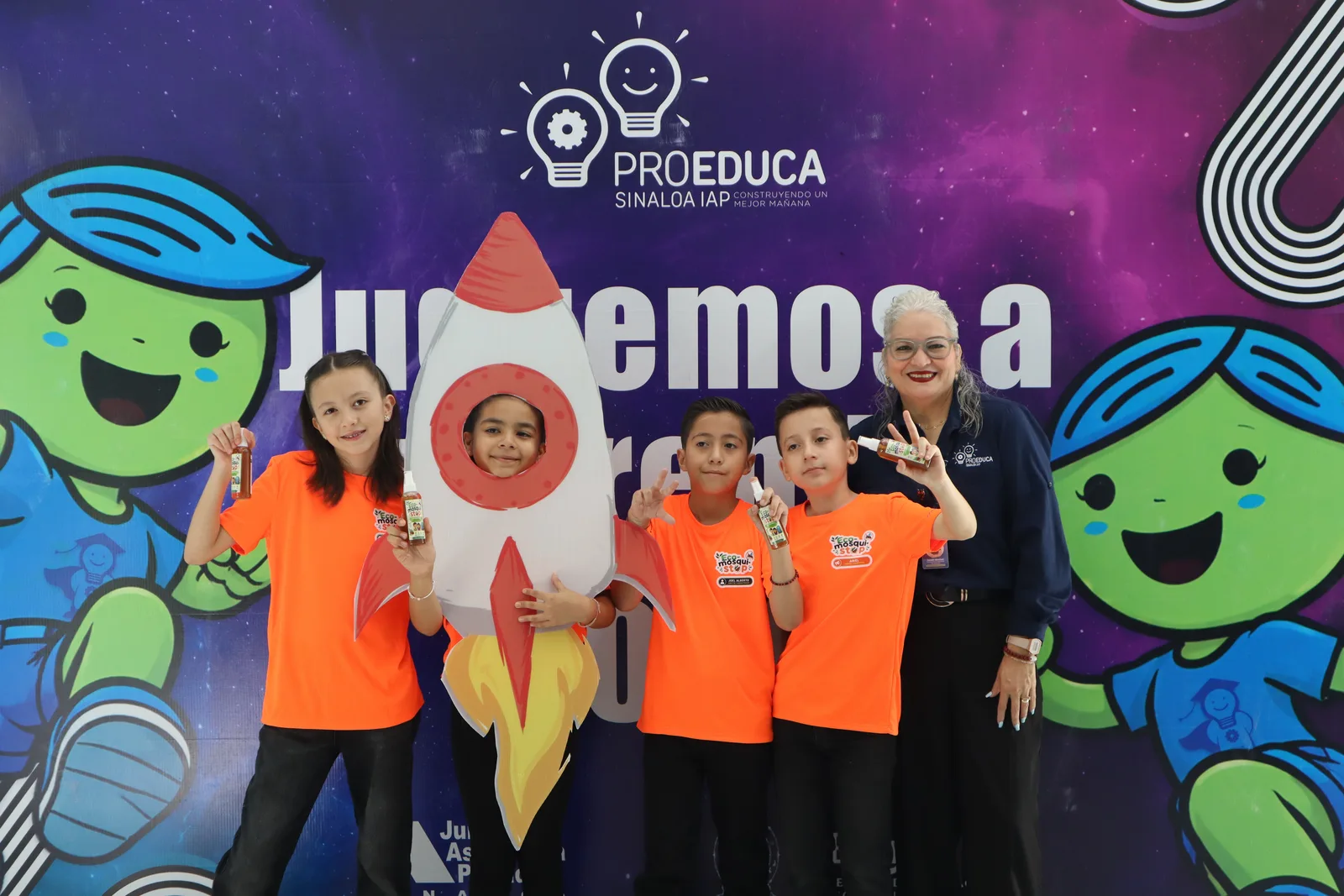 Niñas, niños y una facilitadora de ProEduca posan junto a un cohete de utilería en Juguemos a Emprender